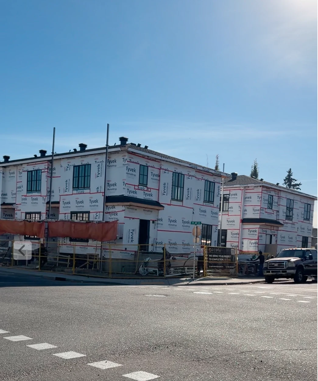Optima multi-family development under construction at 2039 38 St SE, Calgary, with building wrap and site fencing visible